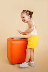 Portrait of a cute funny little girl posing in studio, isolated beige background.