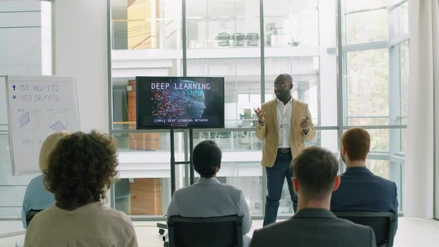 Zoom in shot of African American young man giving lecture to wide audience of people using whiteboard and display on stand