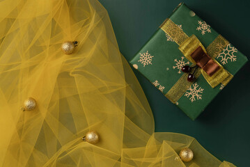 Top view of green Christmas box with gold balls on a yellow tulle. Christmas, New year concept