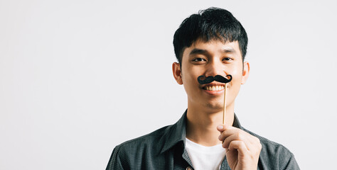 An Asian man's portrait captures his cheerful expression while holding a funny mustache card. Isolated on white, it symbolizes joy and humor for Fathers Day and November.