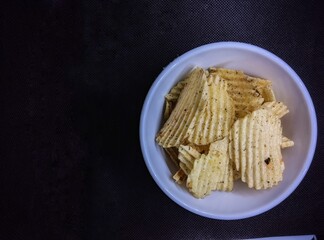 Seaweed-flavored potato chips in a small white bowl. perfect for a casual snack. the picture is taken from a bird's eye view, isolated against a black background.