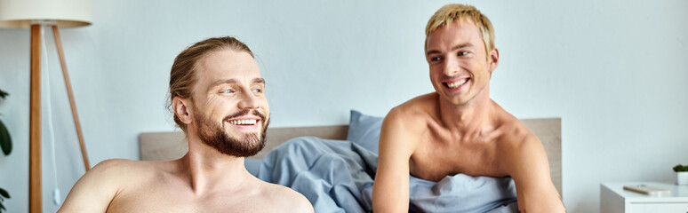 cheerful gay couple smiling in cozy bedroom in morning, serenity and harmonious relationship, banner