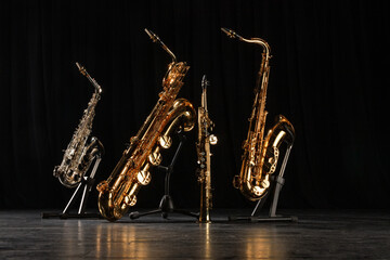 Four different saxophones on stands. Golden, silver and straight saxophones on the black floor of...