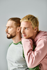 romantic dreamy gay couple in trendy casual attire looking away on grey backdrop, harmony and love