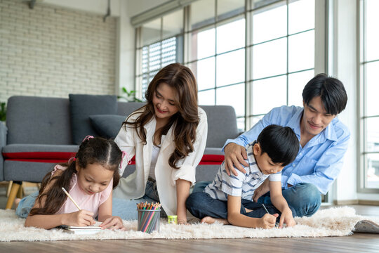 Parents encourage and have fun with their children practicing drawing on the living room floor.