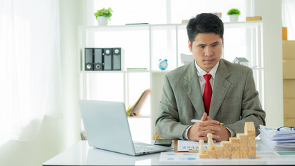 Young Asian businessman checks company budget report graph. Assigned accounts receivable production control Business risk concept with wooden blocks in front