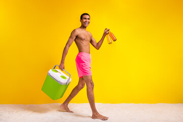 Full length photo of excited positive shirtless man holding refrigerator inviting drink beer empty space isolated yellow color background