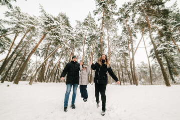 Fototapeta na wymiar Mom, dad throws up child, playing in snow. Family in warm wear having fun and walking in winter forest. Father, mother, kid running in snowy woods, enjoying snowfall in park. Happy winter holidays.