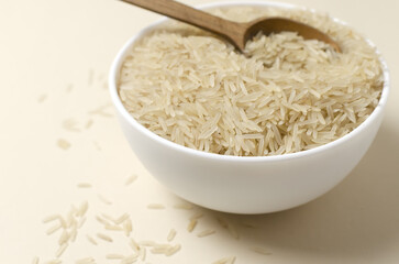 Raw basmati rice in a white bowl with a wooden spoon on a light background. Concept of Water-Conserving Products. Saving water. Dietary product. Healthy Eating. Horizontal orientation. Copy space.