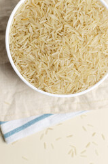 Raw basmati rice in a white bowl with a wooden spoon on a light background. Concept of Water-Conserving Products. Saving water. Healthy Eating. Vertical orientation. Top view. Copy space.