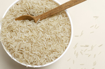 Raw basmati rice in a white bowl with a wooden spoon on a light background. Concept of Water-Conserving Products. Saving water. Vegetarian and vegan food. Horizontal orientation. Top view. Copy space