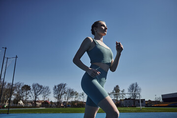 Fototapeta na wymiar low angle view of sportswoman in active wear running outdoors, motivation and sport concept