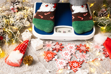 A woman in Christmas socks stands on the scales, weighs herself after gluttony during the holidays