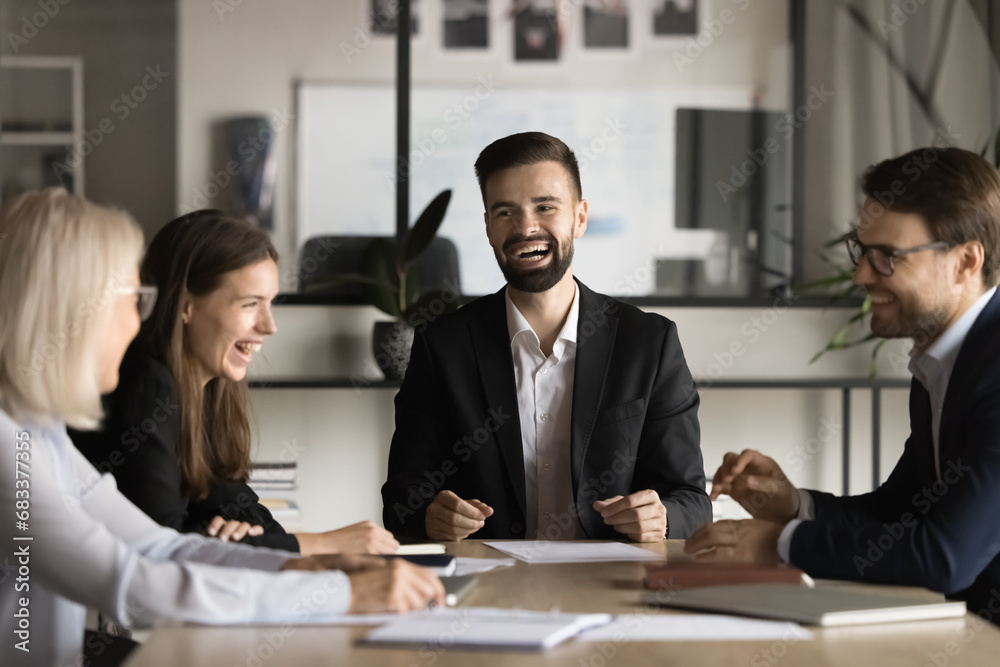 Poster Positive excited business team and young male leader having fun on corporate table, discussing creative ideas, laughing out loud, relaxing, enjoying creativity, funny break at meeting table