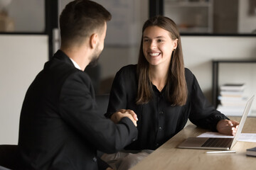 Couple of cheerful business partners shaking hands at workplace, smiling, discussing cooperation, partnership, ending negotiation, consultation meeting. Happy customer girl giving handshake to manager