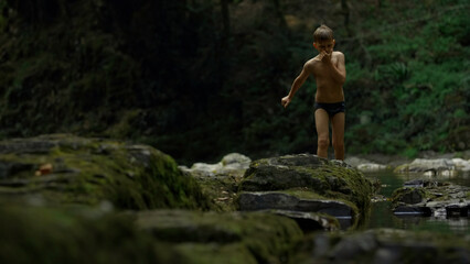 Fototapeta na wymiar Boy walking on mossy rocks on green hills background. Creative. Teenager boy in jungles.