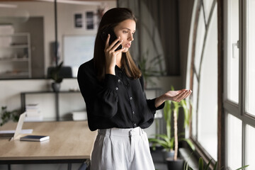 Serious young business woman talking on mobile phone in office, discussing work project, problem solving, work solutions, speaking on smartphone, making professional telephone call