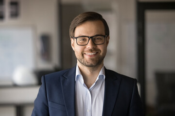 Cheerful successful business professional man in stylish eyeglasses and office suit looking at camera, smiling, posing for professional portrait. Confident boss, business leader video call head shot
