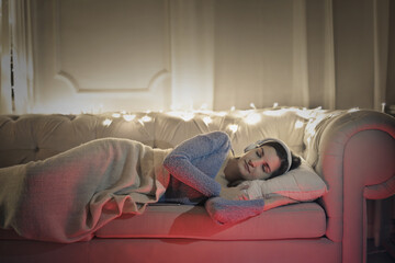 young woman rests lying on a sofa while listening to music