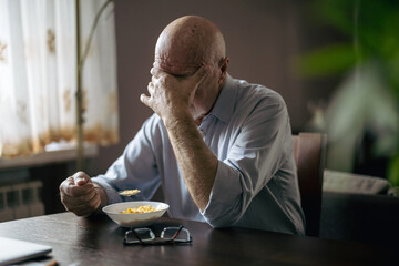 Depressed senior man eating breakfast alone at home
