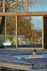 Woman unwinds in a jacuzzi on a wooden deck, framed by a modern cabin