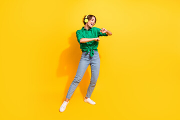 Fototapeta na wymiar Full length photo of cheerful positive girl dressed green shirt headphones having fun isolated yellow color background