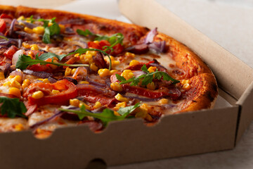 Large Pizza with sausages peppers and sweetcorn in open carton box on kitchen table extreme closeup view