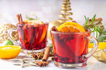 Traditional Christmas aromatic mulled wine cocktail, red wine grog tea drink with spices, cinnamon, orange and rosemary sprig, on Christmas New Year decorated wooden cozy background