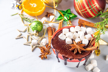 Winter aromatic hot chocolate cup with Christmas background. Mug of dark hot cocoa drink with cinnamon, anise, spices and marshmallow, on cozy Christmas and New Year holiday decorated background 