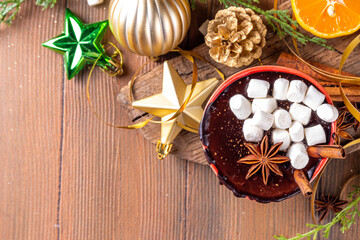 Winter aromatic hot chocolate cup with Christmas background. Mug of dark hot cocoa drink with cinnamon, anise, spices and marshmallow, on cozy Christmas and New Year holiday decorated background 