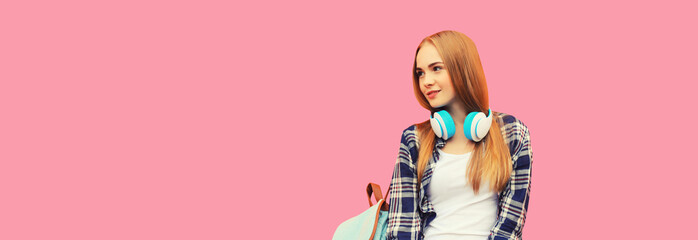 Portrait of happy smiling teenage girl in wireless headphones listening to music looking away on pink studio background, blank copy space for advertising text