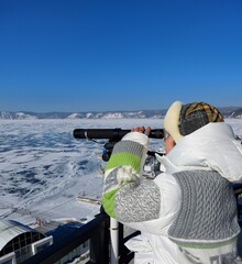 A tourist looks through a telescope at the mountains and ice. Winter Baikal.