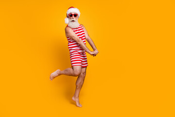 Full length photo of cheerful impressed senior guy christmas swimwear hat glasses dancing having fun empty space isolated yellow color background