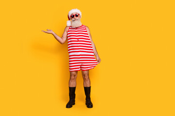 Full length photo of funny cheerful senior guy dressed christmas swimwear hat glasses showing arm...