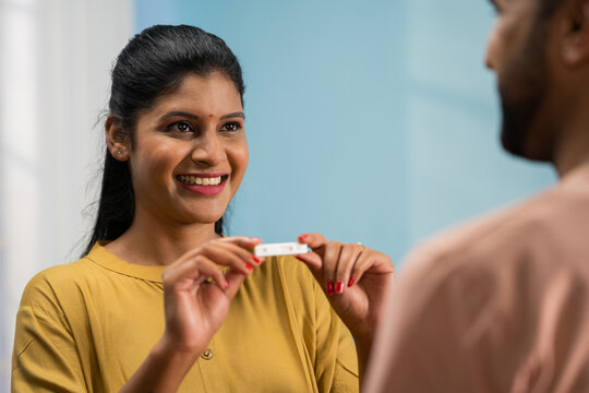 Shoulder shot of excited Indian wife showing positive pregnancy test to husband by hugging at home - concept of Anticipating parenthood, Shared happiness and happy news