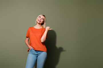 Photo portrait of pretty young girl posing point empty space billboard dressed stylish orange outfit isolated on khaki color background