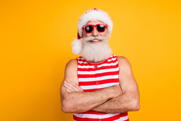 Photo of funky cheerful senior guy dressed christmas swimwear hat glasses arms crossed enjoy vacation isolated yellow color background - obrazy, fototapety, plakaty