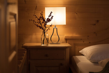 A cozy corner in a hotel room, on the bedside table there is a dimmed lamp and a bouquet of...