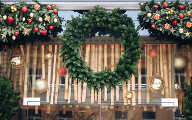 A beautiful round natural Christmas wreath made of fir branches with toys hangs on a glass display case with bamboo. Lviv, Ukraine.