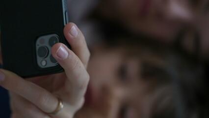 Close-up of mother and child looking at cellphone device screen laid in bed. Parent and son...