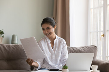 Young happy Indian woman read paper notification from bank looks overjoyed get great news about...