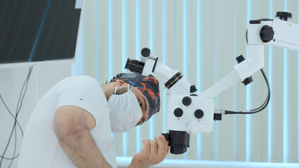 Ophthalmological surgery specialist in front of microscope before operation. Action. Side view of male doctor with medical equipment. - obrazy, fototapety, plakaty
