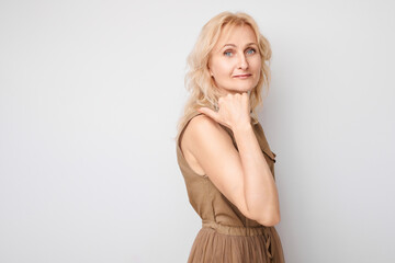 Fototapeta premium Beautiful mature woman 50 years old pointing finger aside, demonstrating empty space for product or text isolated on white studio background