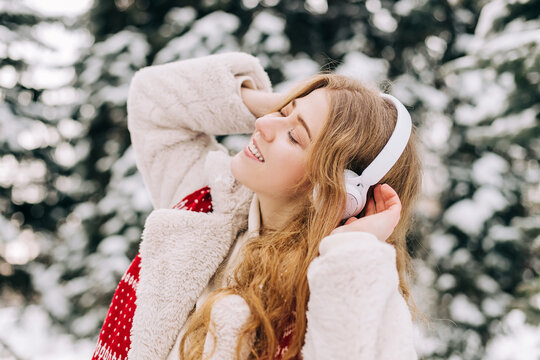 Young woman dressed in a red Christmas scarf listening to music outdoors in winter