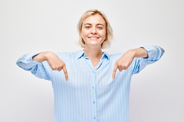 Young blond woman in casual pointing down finger, demonstrating empty space for product or text isolated on white studio background.