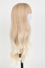 Obraz premium Natural looking blonde wig on white mannequin head. Long hair on the plastic wig holder isolated on white background, side view.