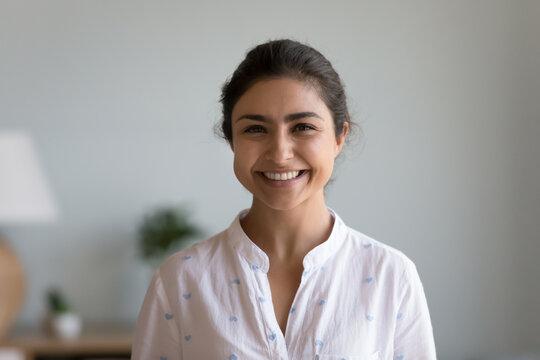 Happy Indian woman posing indoors looking at camera. Beautiful female having wide white toothy smile advertise professional dental services. Young housewife or applicant head shot portrait concept