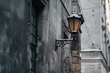 Medieval metal black street lamp on the wall along a winter street in Lviv. Vintage retro lantern on the facade of a house covered with snow.