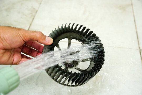 Hands man technician using water hose to clean dirty car fan blower motor cage (squirrel cage), cleaning process on white floor tiles background with copy space for maintenance or service concept.