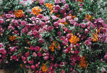 Lots of purple and orange artificial rose flowers and green leaves. Natural background.